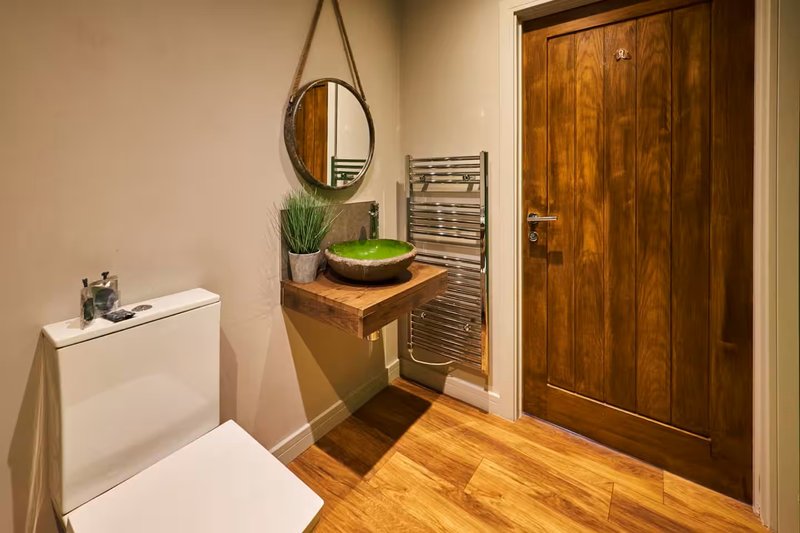 Hallway with wooden flooring, round mirror, potted plant, wooden door and white radiator