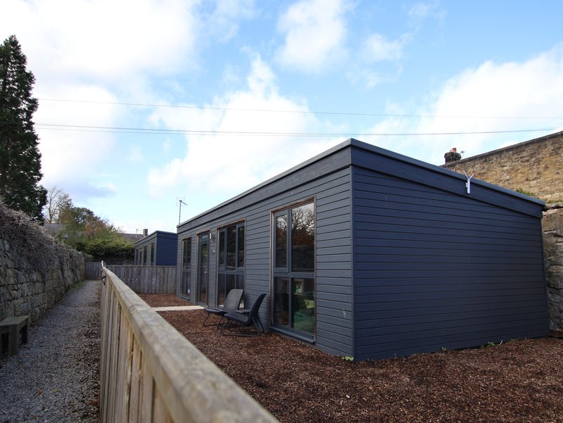 Modern dark-clad garden building with large windows, gravel courtyard and wooden fence