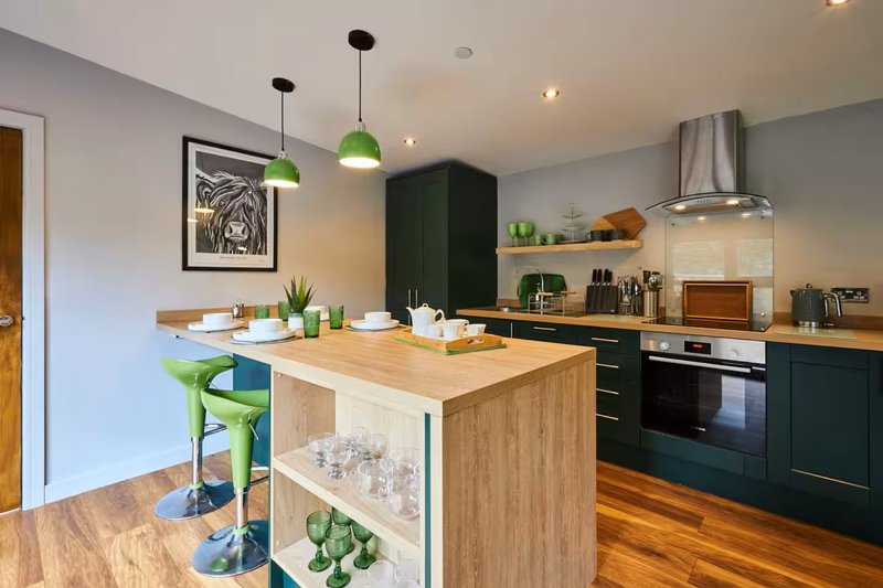 Modern kitchen with wooden island, green pendant lights, dark cabinetry and stainless steel appliances