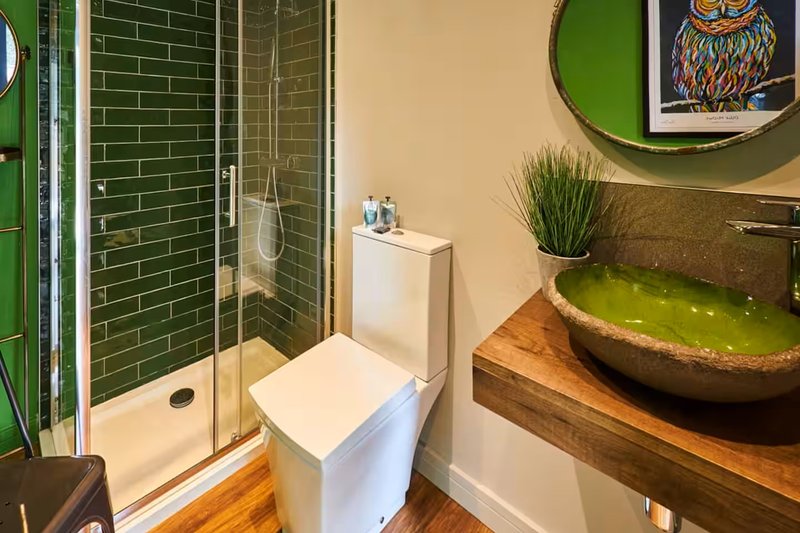 Modern bathroom with green tile shower, white toilet, wooden vanity and round mirror