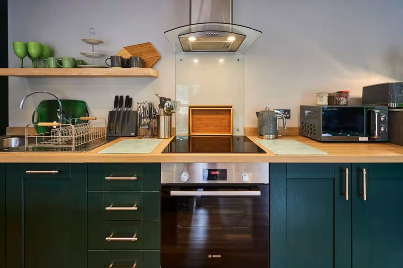 Modern kitchen with dark green cabinetry, wooden countertop, stainless steel appliances and open shelving