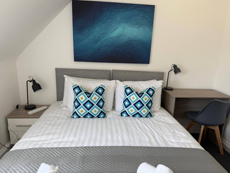 Modern bedroom with gray upholstered bed, blue patterned cushions, bedside tables and abstract wall art
