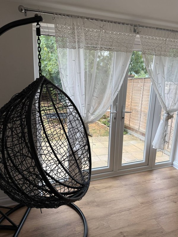 Modern living room with black hanging egg chair, sheer curtains, and sliding doors to garden