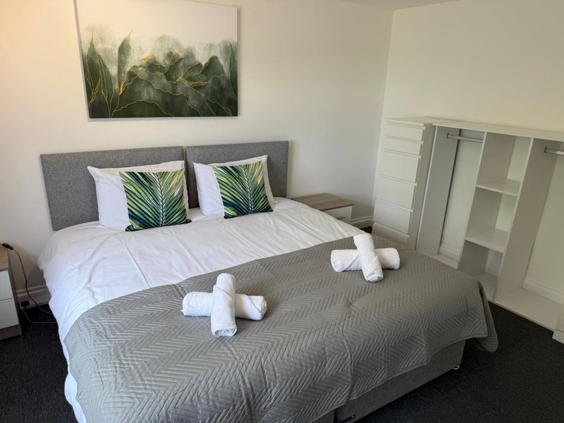 Modern bedroom with gray upholstered bed, white bedding, green cushions and rolled towels