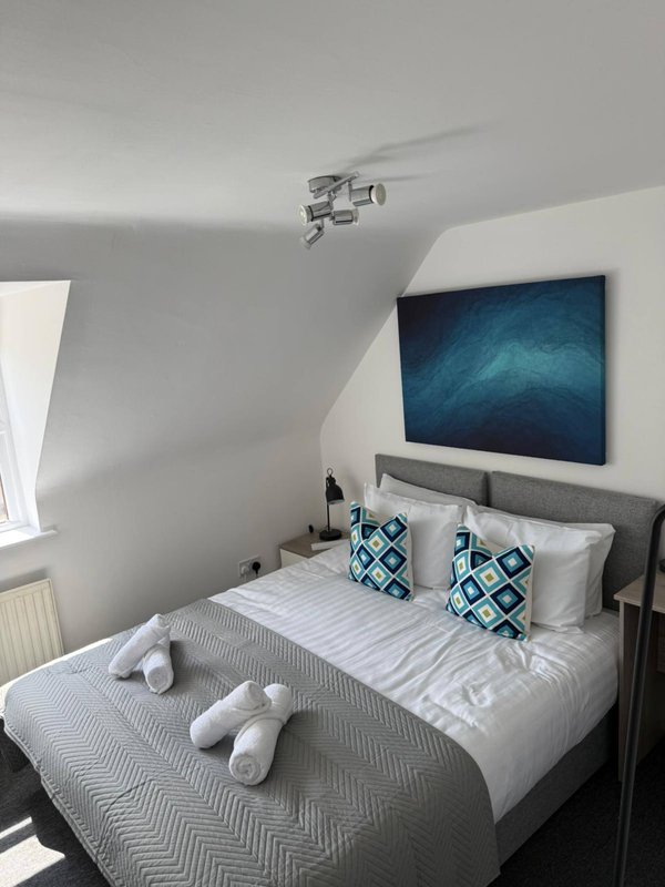 Modern bedroom with double bed, grey headboard, wall-mounted TV and blue patterned cushions