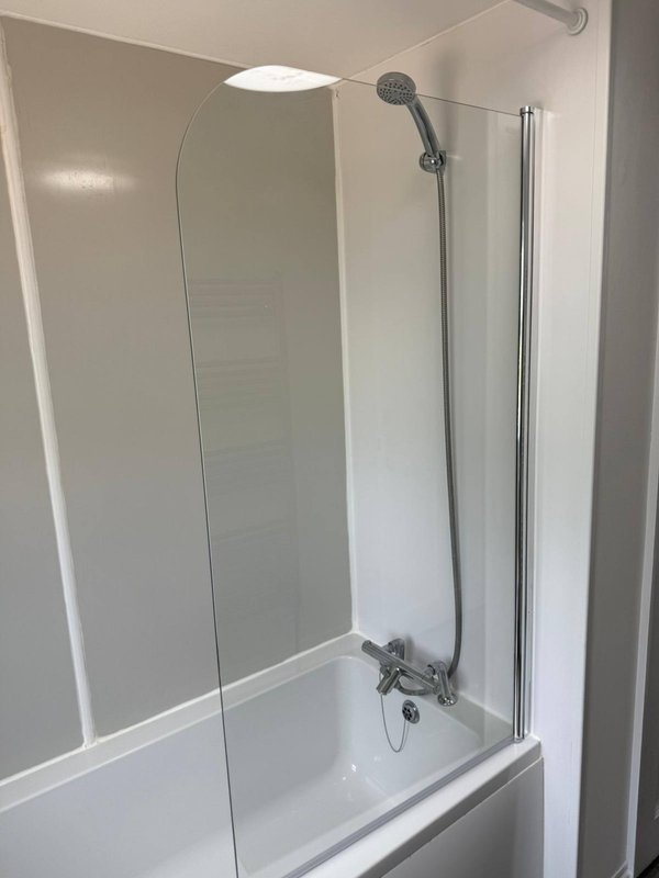 Modern bathroom with white bathtub, glass shower screen, chrome fixtures and showerhead