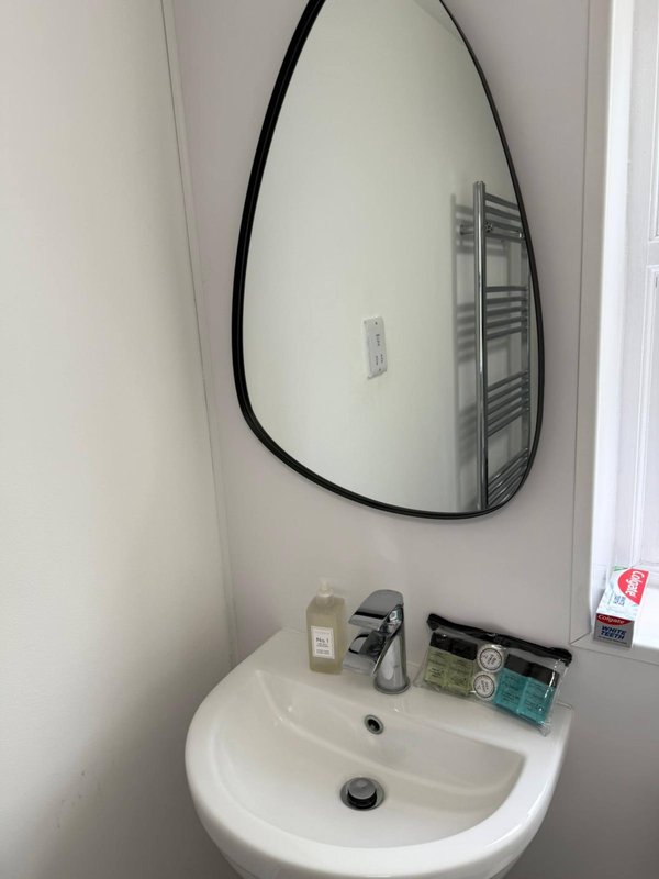 Bathroom corner with white wall-mounted sink, round mirror with black frame, and toiletries
