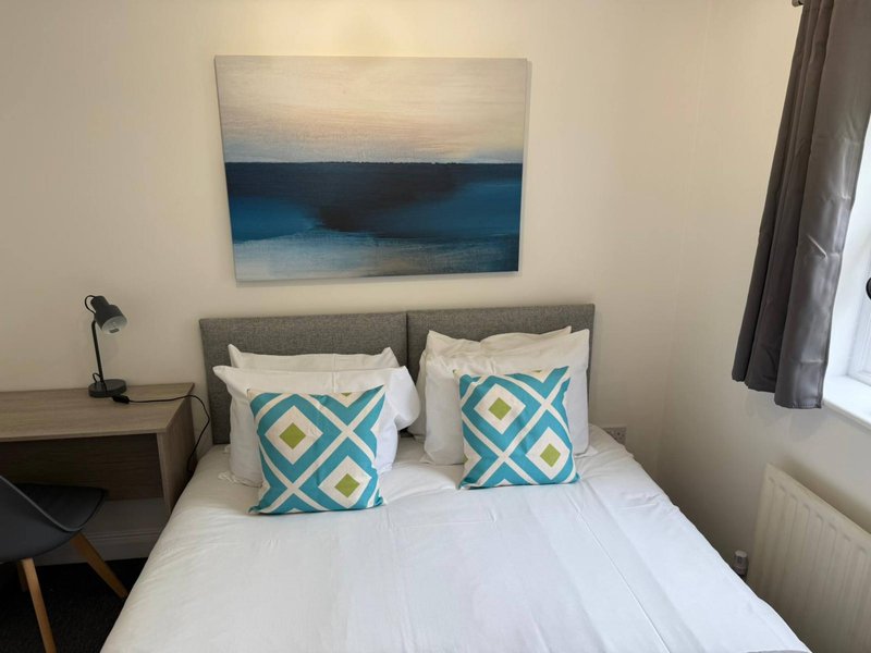 Bedroom with double bed, patterned cushions, bedside lamp and abstract artwork