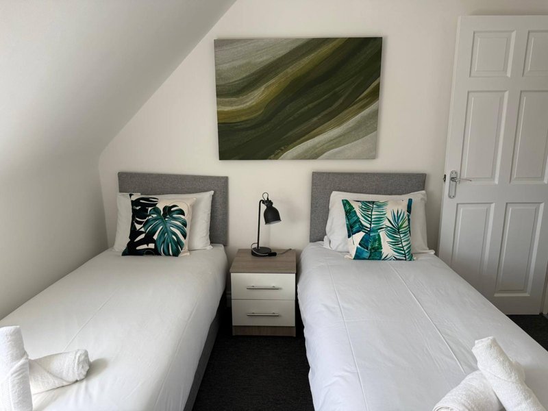 Twin bedroom with two single beds, grey headboards, white bedding, and tropical-themed cushions