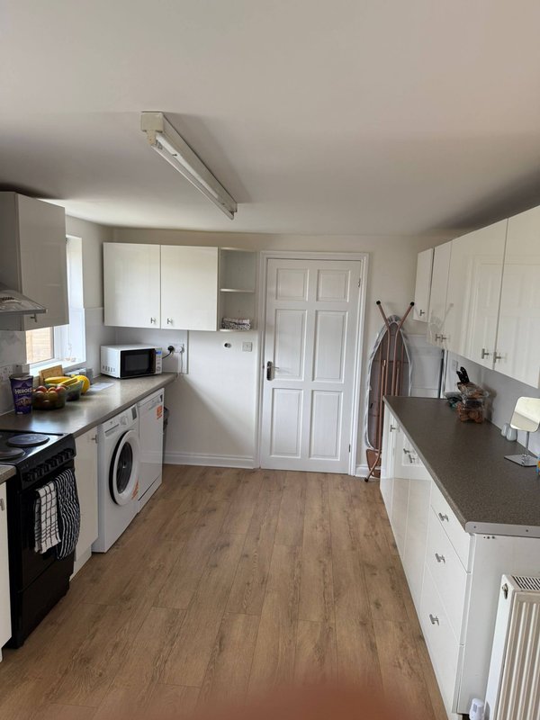 Galley kitchen with white cabinetry, black range cooker, washing machine and wooden flooring