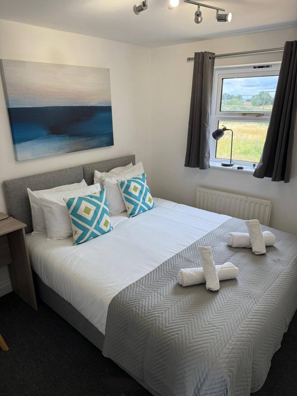 Bright bedroom with double bed, patterned cushions, abstract wall art, and countryside view from window