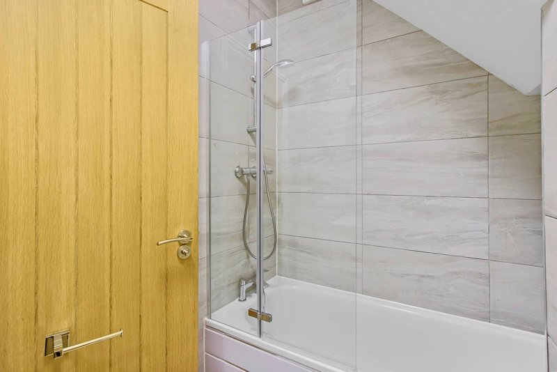 Modern bathroom with wooden door, tiled shower enclosure and white bathtub
