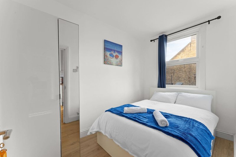 Bright bedroom with double bed, blue throw, window with blue curtains, and wooden flooring