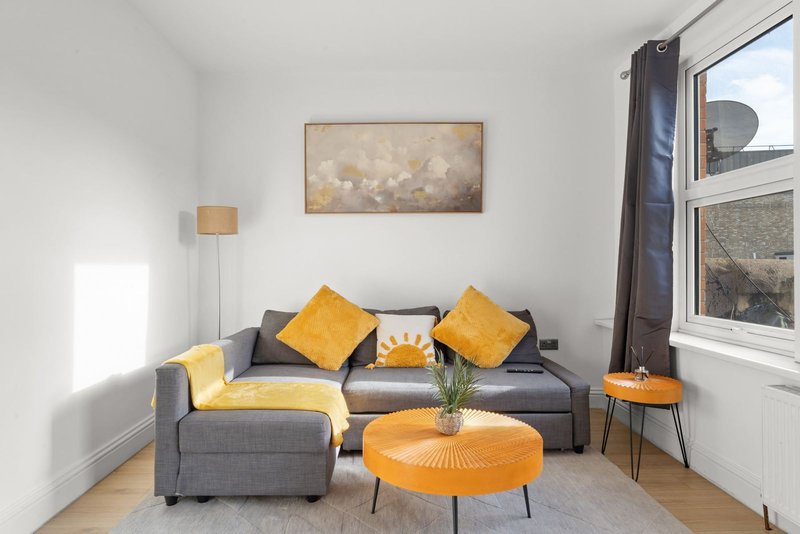 Bright living room with gray sofa, yellow cushions, orange coffee table and wall art