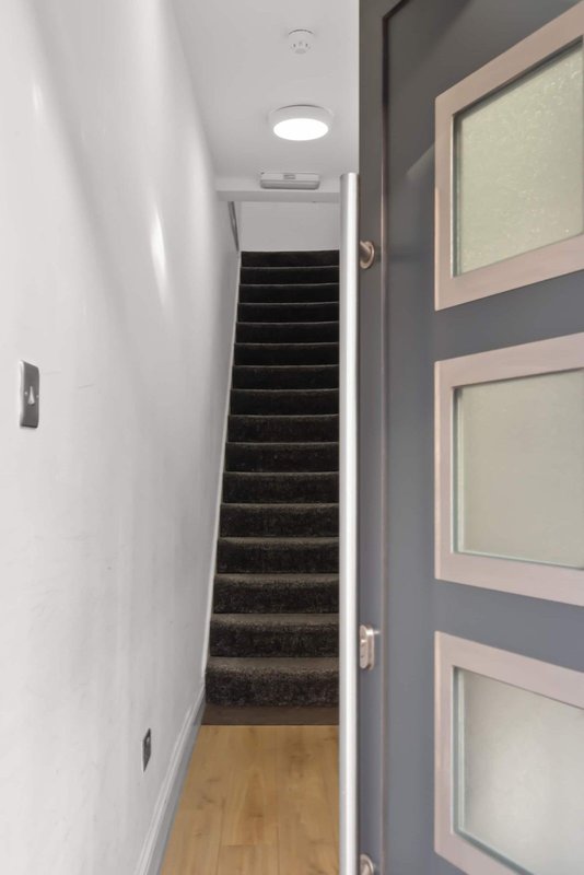 Staircase with black treads, white walls, wooden floor landing, and framed artwork on door