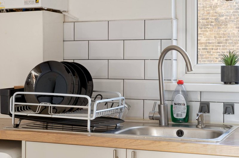 Kitchen counter with sink, faucet, dish rack, and cleaning supplies