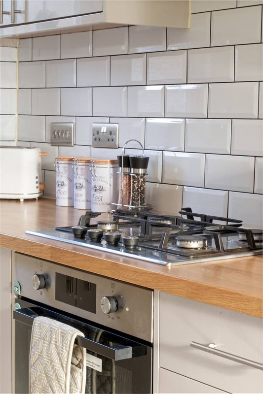 Kitchen with gas cooktop, wooden counter, white subway tile backsplash and cooking utensils