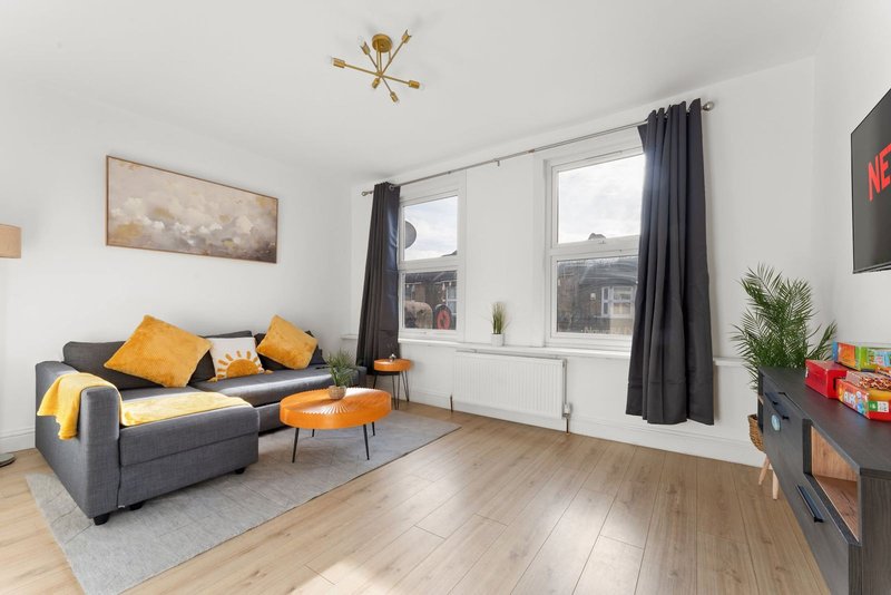 Modern living room with grey sofa, orange accents, wooden flooring and large windows
