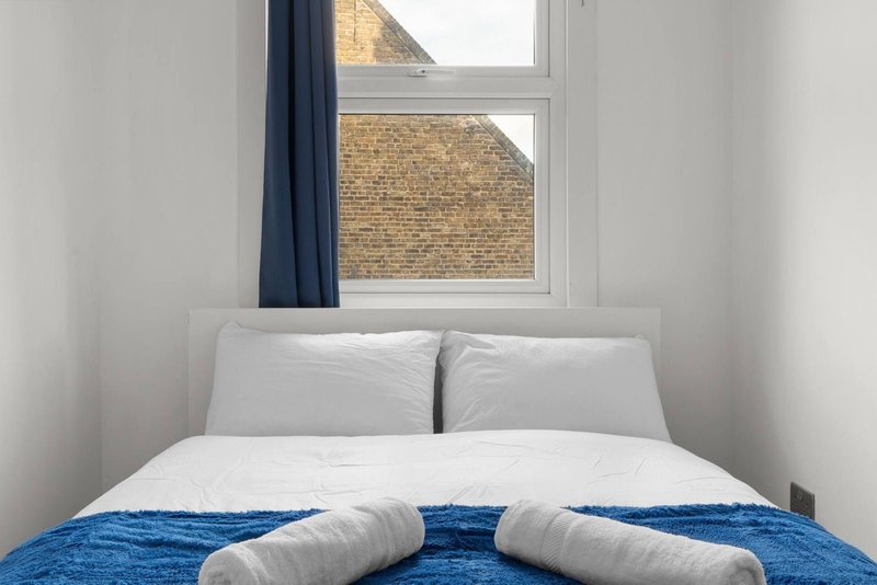 Bedroom with double bed, white pillows, blue blanket and window with brick view