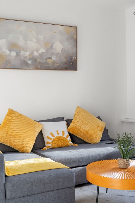 Modern living room with gray sofa, yellow cushions, abstract wall art, and orange side table