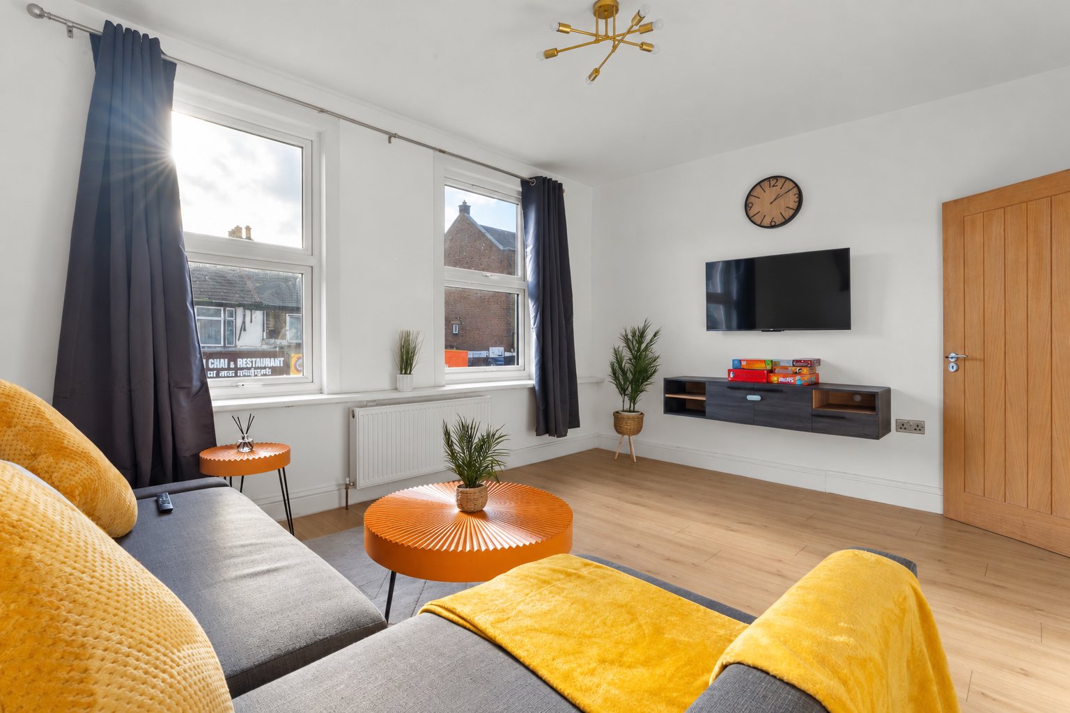 Bright living room with grey sofa, yellow armchairs, wooden floor and wall-mounted TV