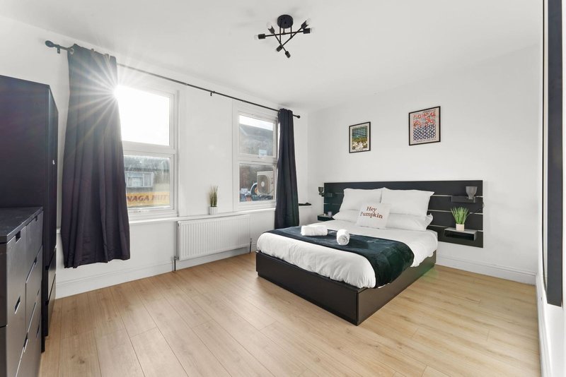 Modern bedroom with double bed, black headboard, wooden floor and large window with dark curtains