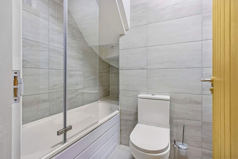 Modern bathroom with combined bath and shower, toilet, and light wood door