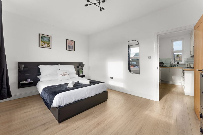 Modern bedroom with black bed, white bedding, wooden floor, and en-suite bathroom