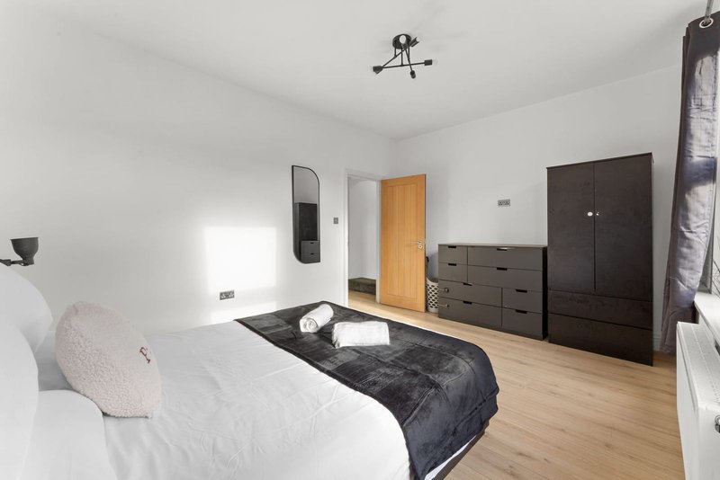 Bright bedroom with double bed, dark wardrobe, wooden door, and wooden flooring