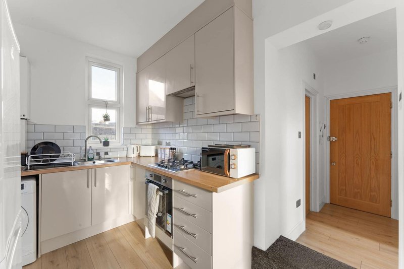 Modern kitchen with white cabinetry, wooden countertop, tiled backsplash and wooden flooring