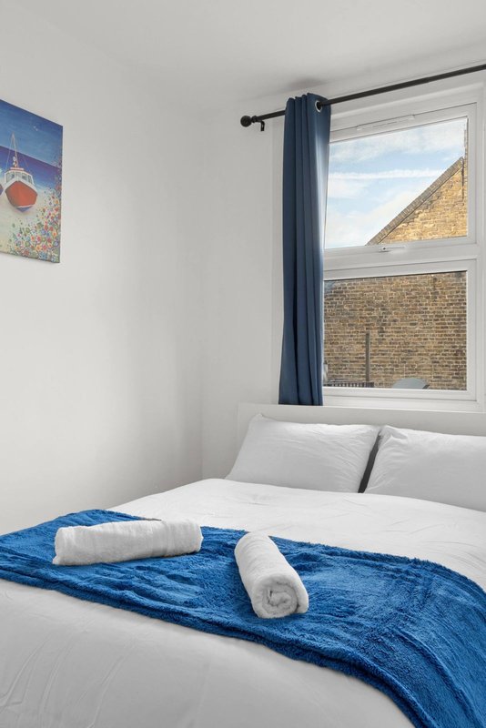 Bright bedroom with double bed, blue throw blanket, white pillows and window overlooking brick building