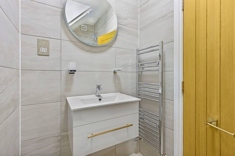 Modern bathroom with white vanity sink, round mirror, heated towel rail and light grey tile walls