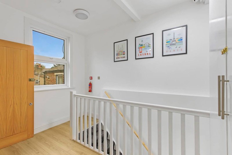 Bright stairwell with white balustrade, wooden door, window with countryside view, and framed prints on wall