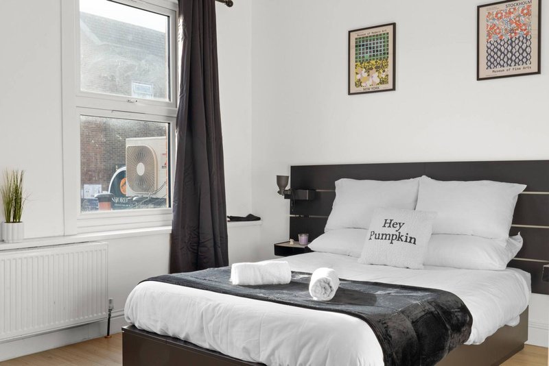 Modern bedroom with double bed, black headboard, white bedding, and large window with curtains