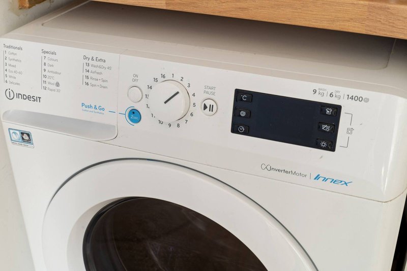 White front-loading washing machine with control panel and wooden shelf above
