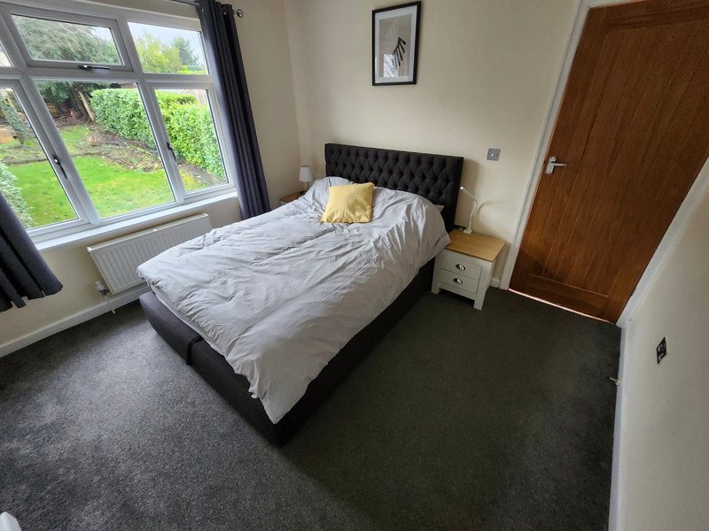 Bedroom with double bed, bedside table, wooden wardrobe and garden view through window