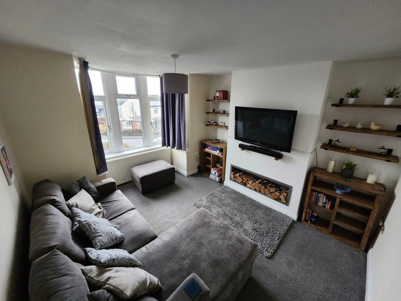 Living room with gray sofa, TV on wall mount, fireplace, shelving, and bay windows