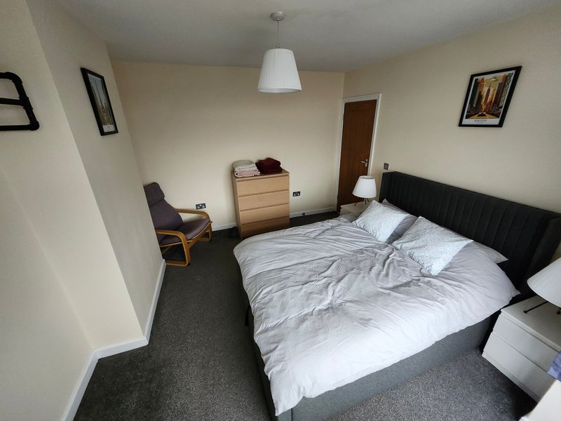 Bedroom with double bed, wooden chest of drawers, armchair, pendant light and framed wall art