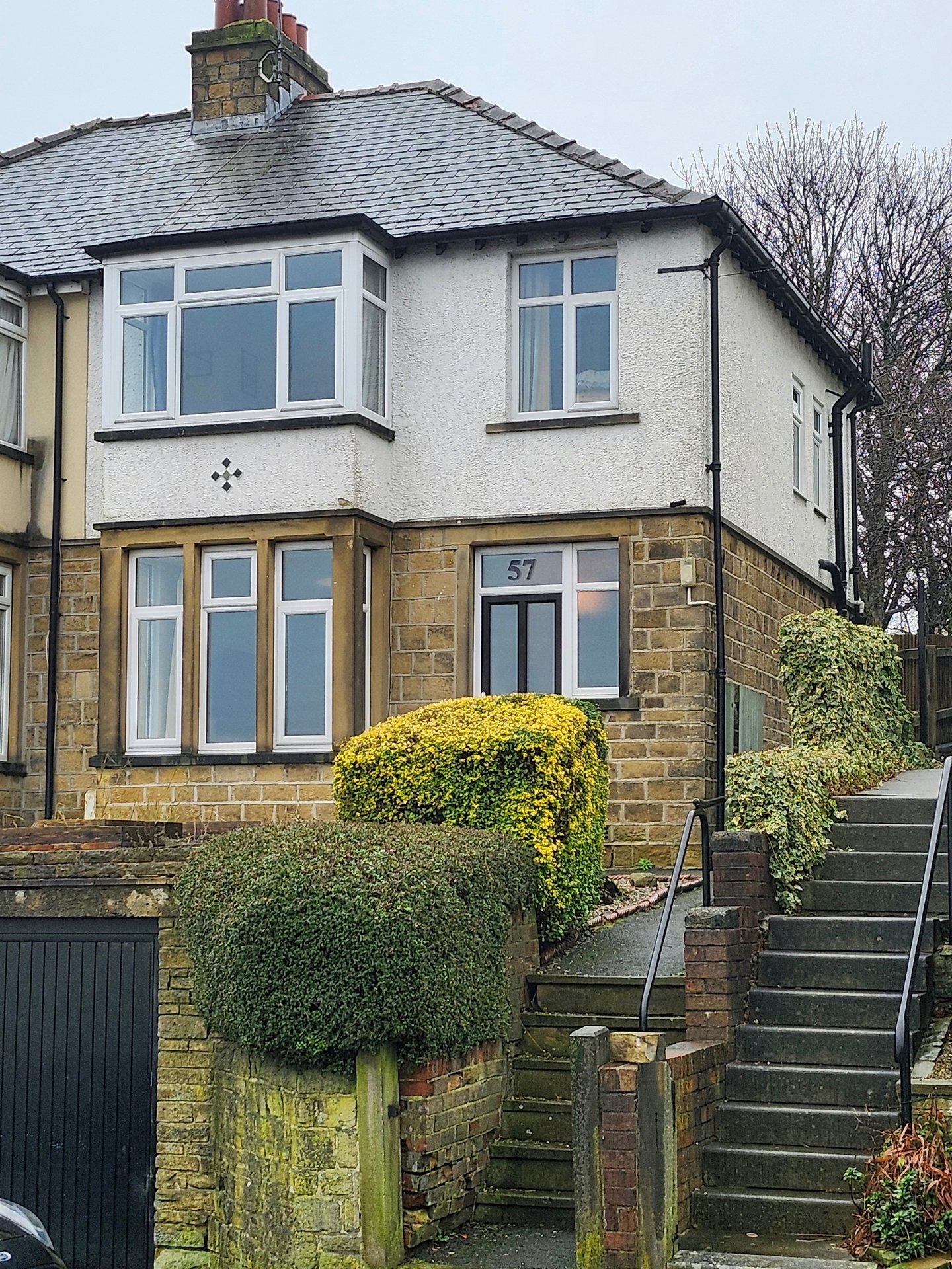 Semi-detached house exterior with white render, bay windows, stone base and front garden