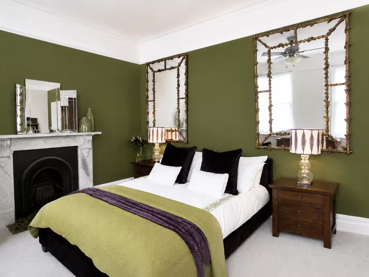Bedroom with olive green walls, fireplace, double bed with yellow throw, and decorative mirrors