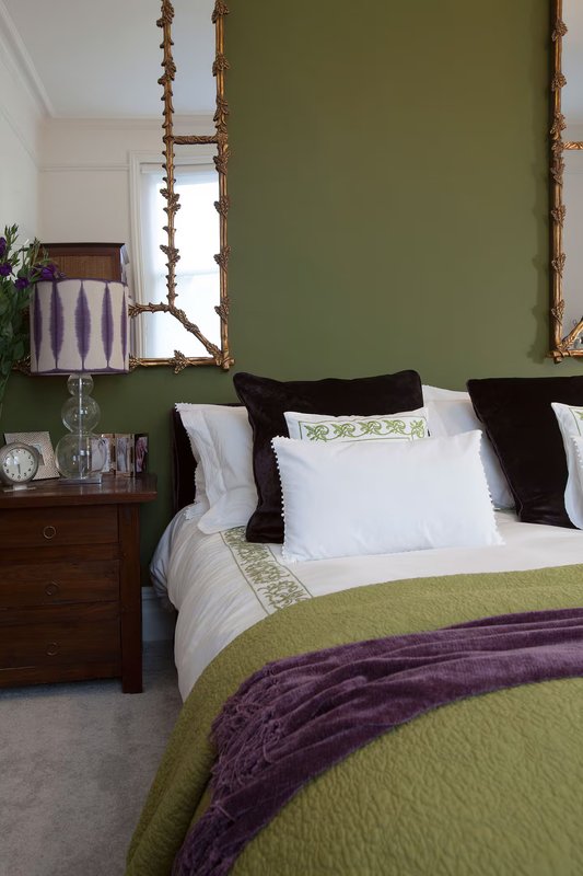 Bedroom with olive-green feature wall, double bed with white and green bedding, wooden nightstand, and decorative wall hanging.