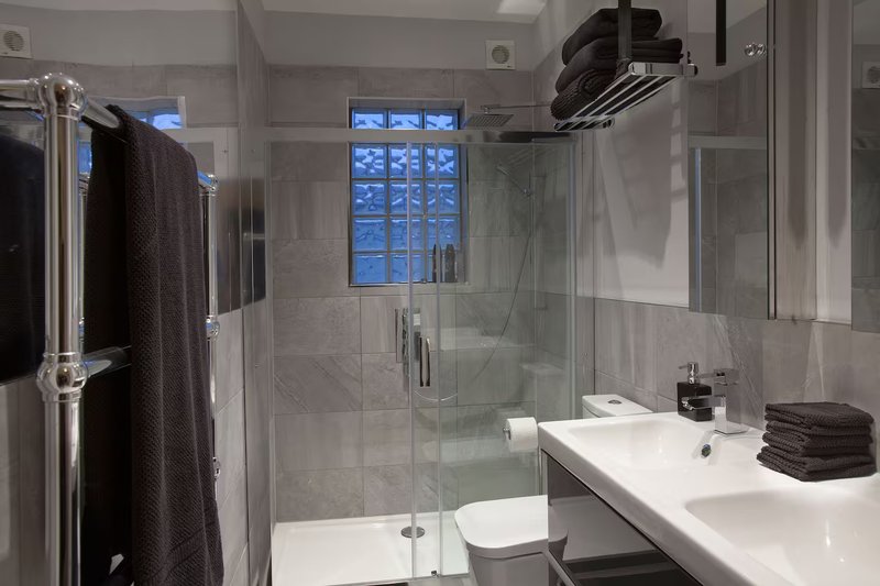 Modern bathroom with walk-in shower, double sink vanity, and dark towels