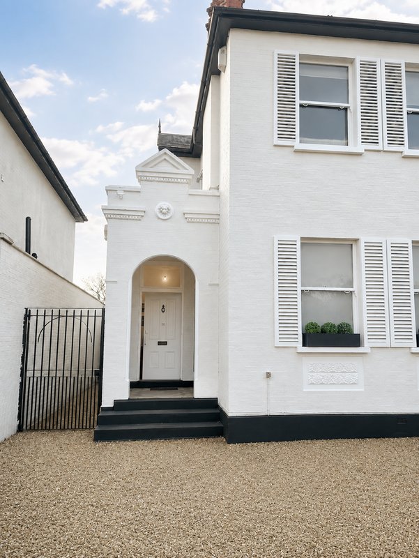 White exterior of detached house with black door, shuttered windows and gravel driveway