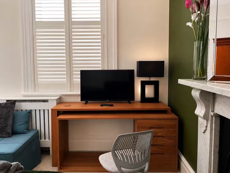 Modern home office with wooden desk, monitor, chair, green accent wall and fireplace