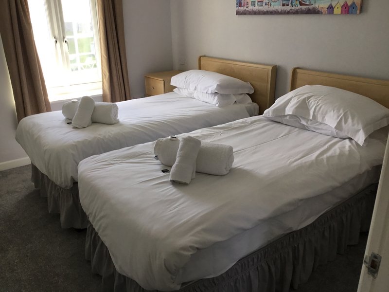 Twin beds with white bedding, rolled towels, wooden headboards and window with curtains