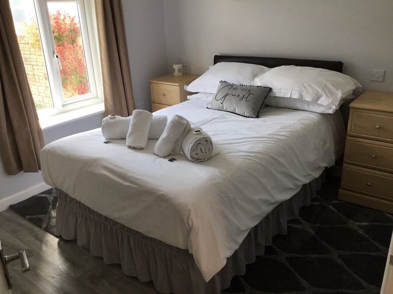 Bedroom with double bed, white bedding, wooden nightstands, window with autumn garden view
