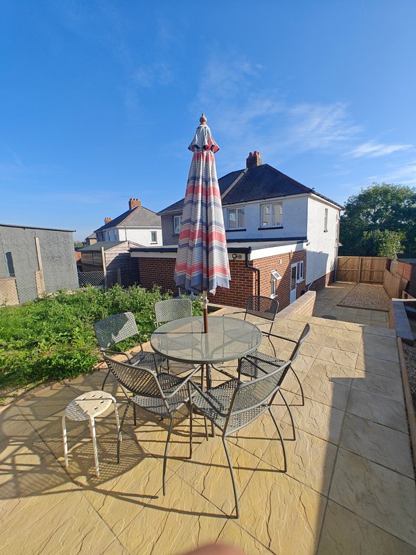 Rear garden patio with table, chairs, parasol and residential properties beyond