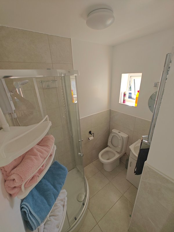 Small bathroom with shower enclosure, toilet, sink and towel rail with folded towels