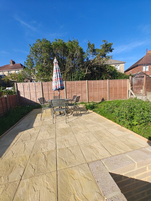 Paved garden patio with table, chairs, and striped parasol under blue sky