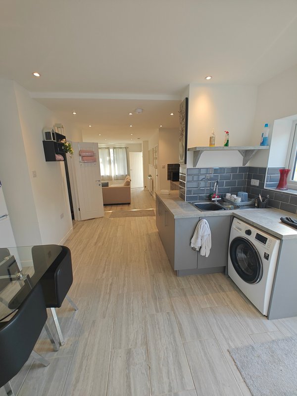 Modern kitchen and living space with washing machine, blue tile backsplash, wooden flooring